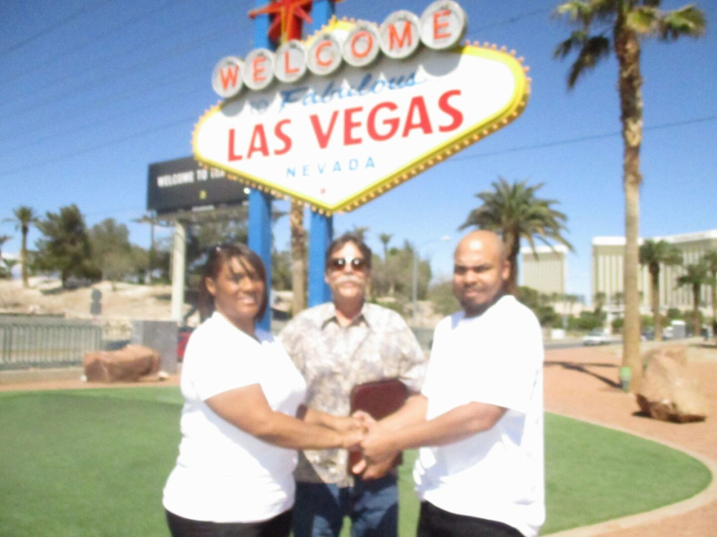 Three people are holding hands in front of a sign.