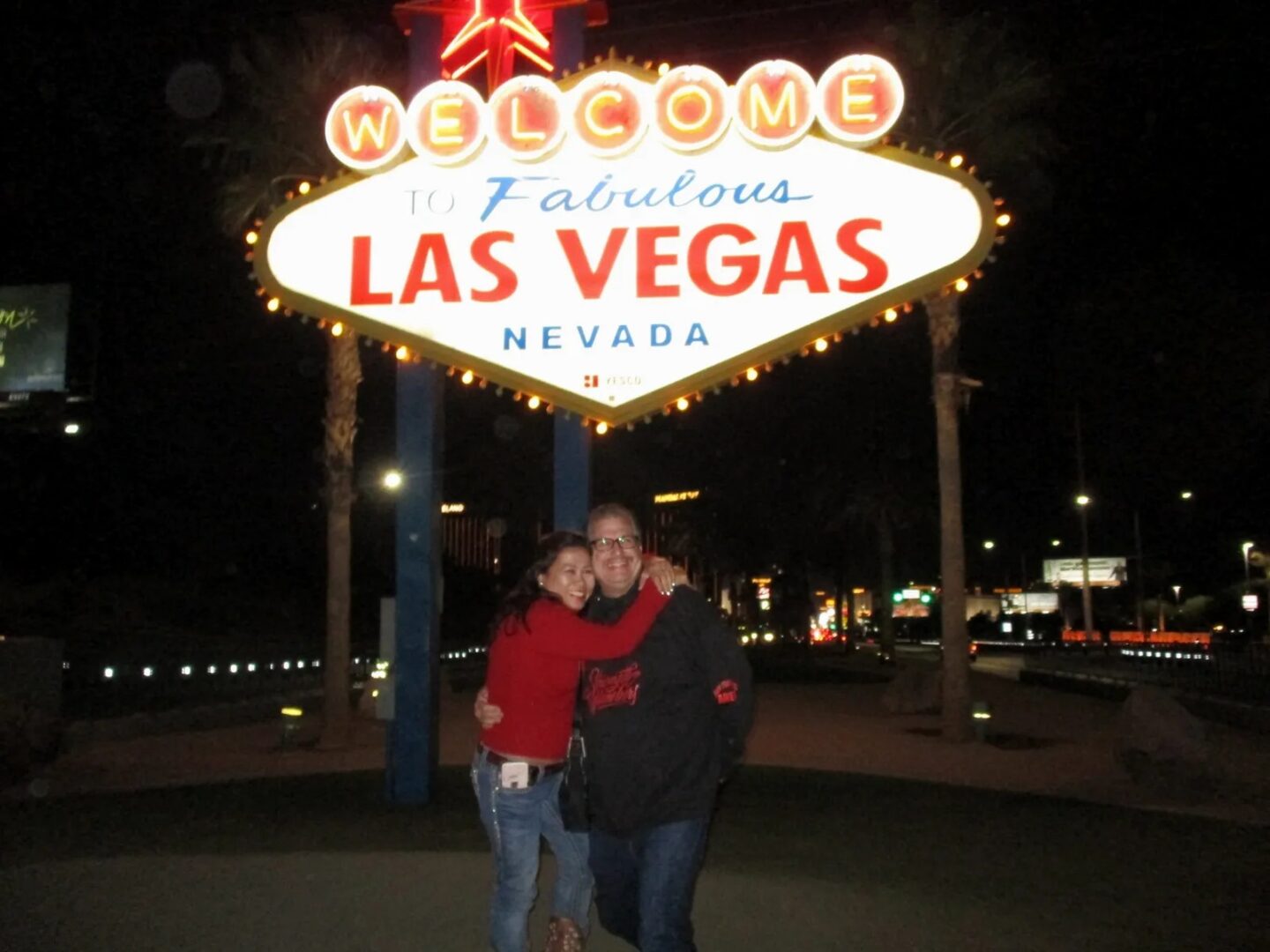 A couple is standing in front of the welcome to las vegas sign.