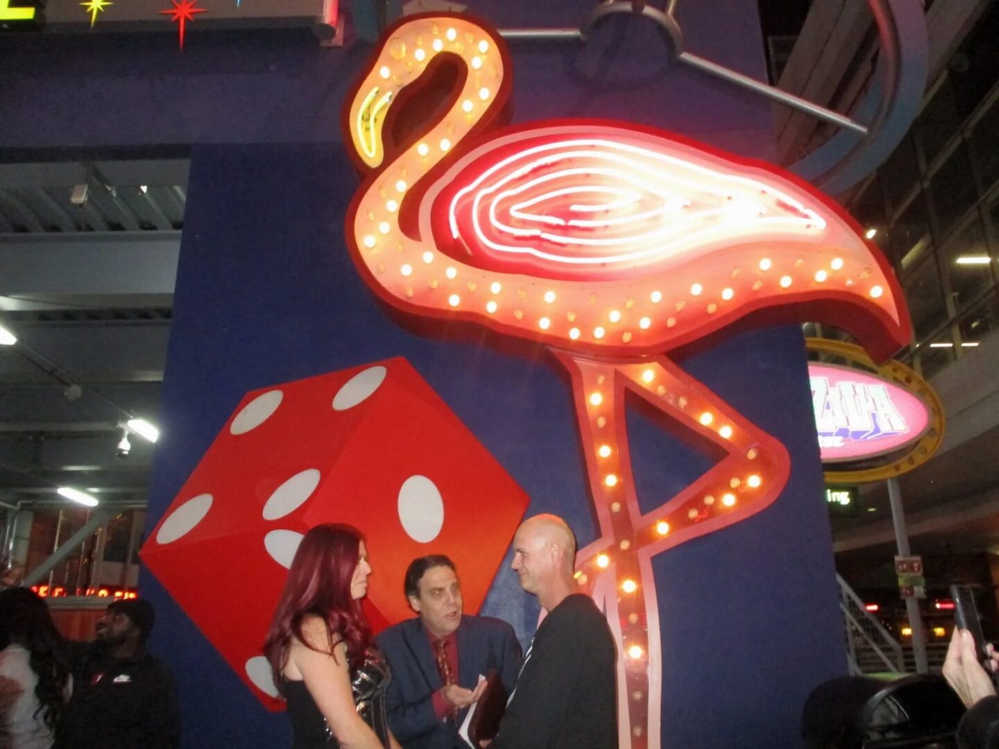 A group of people standing around a neon flamingo.